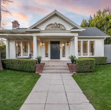 Front view of a charming white house with columns, a manicured lawn, and a cloudy sunset sky in the background