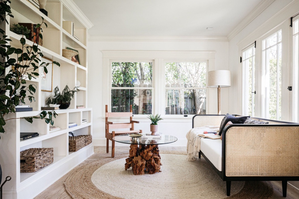 Bright living room with large windows, a beige sofa, round glass coffee table, and built-in shelves filled with decor.