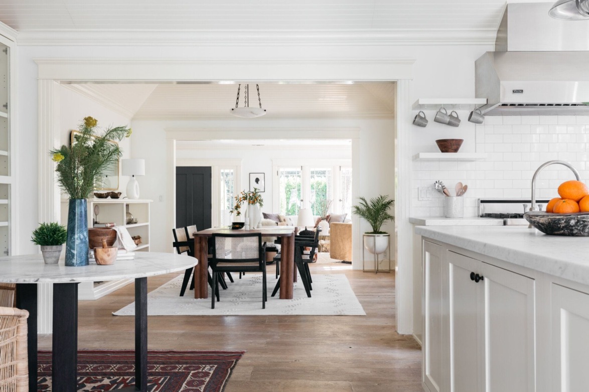 Modern open kitchen and dining area with white cabinetry, wooden table, and bright natural lighting.