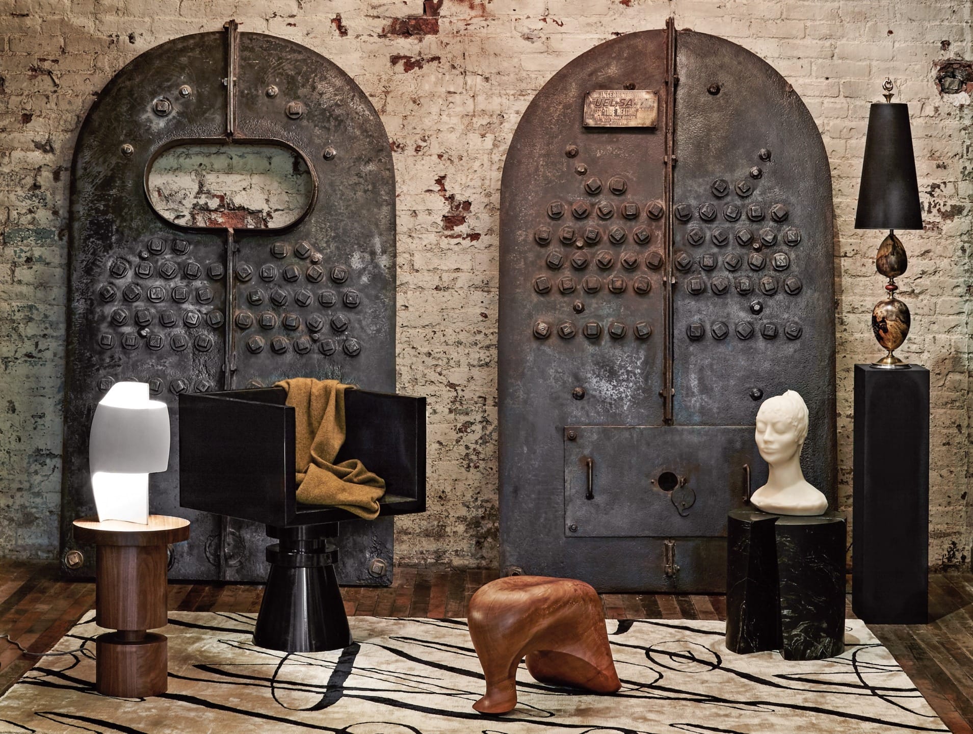 Industrial-style room with rustic metal doors, modern furniture including a sculptural chair, lamps, and decorative bust.