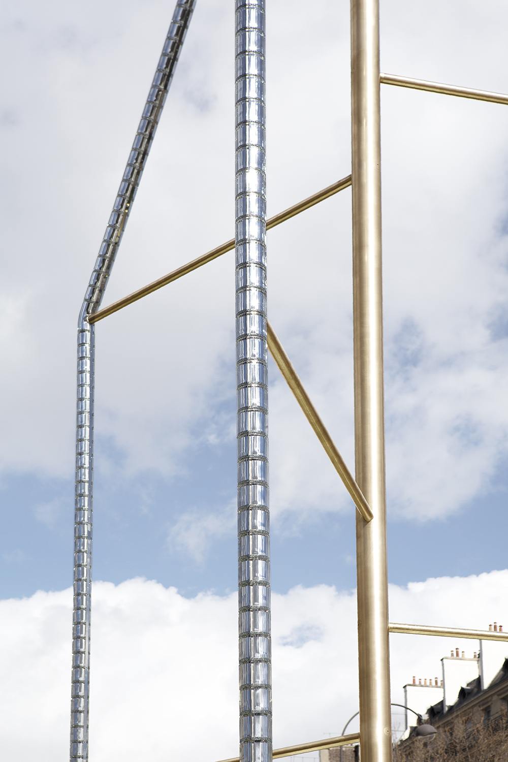 Metallic sculpture against a cloudy sky background, featuring vertical and diagonal rods with a minimalist design.