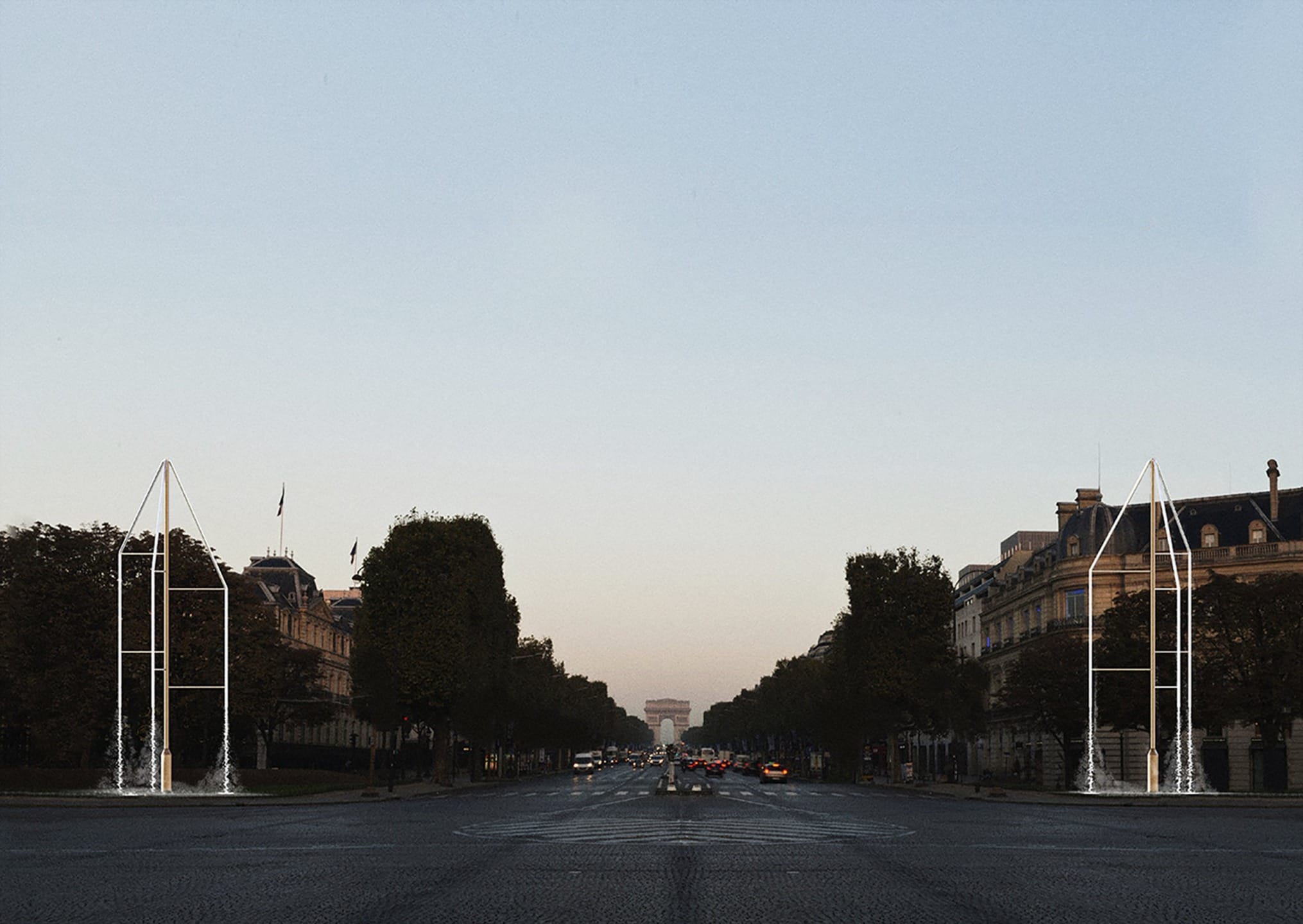 Wide city boulevard at dusk with trees lining the street and distant view of a triumphal arch.