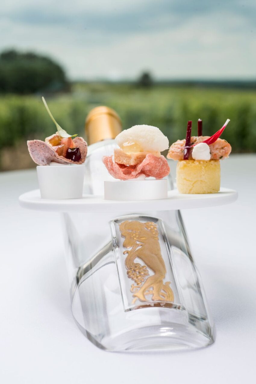 Elegant wine bottle with gourmet appetizers on top, set against a blurred natural background.