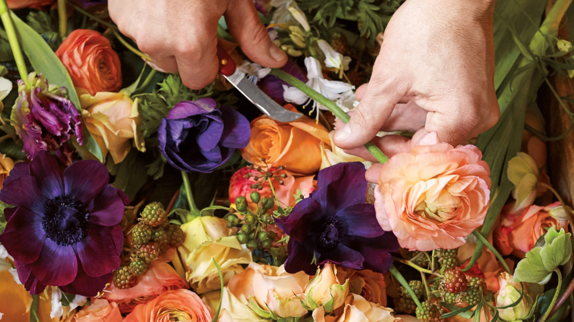 Hands arranging colorful flowers with scissors.