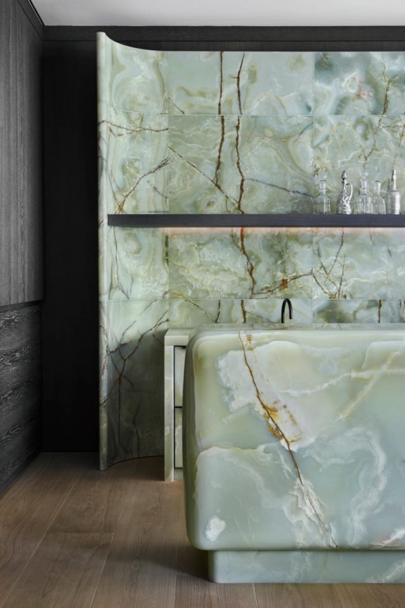 Luxury bathroom with green marble walls and sink, featuring sleek dark wood paneling on the side.