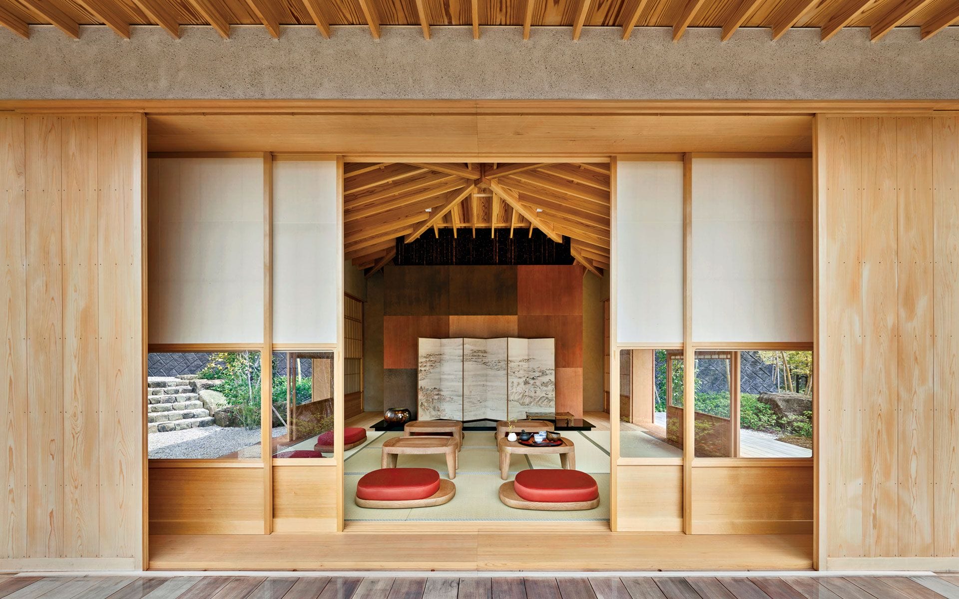 Traditional Japanese room with sliding doors, tatami mats, red cushions, and a decorative screen, showcasing minimalist design.