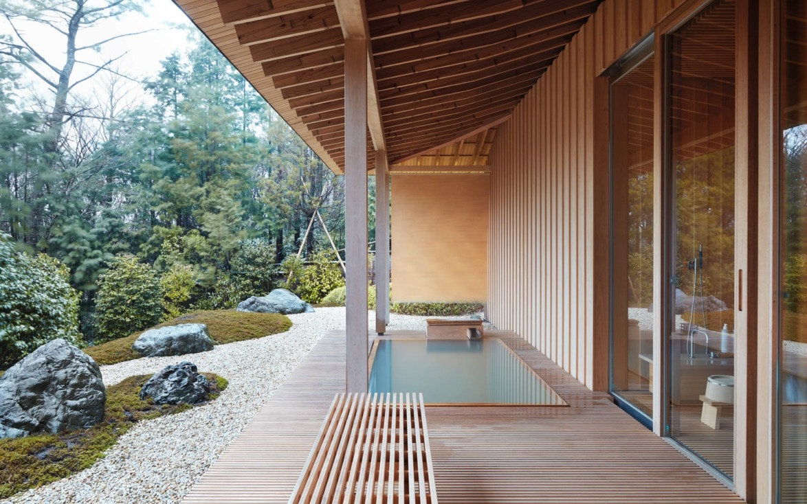 Japanese-style wooden terrace with water feature and garden view, featuring rocks and lush greenery.