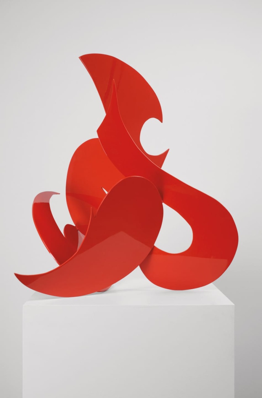 Abstract red sculpture on display stand against a plain background