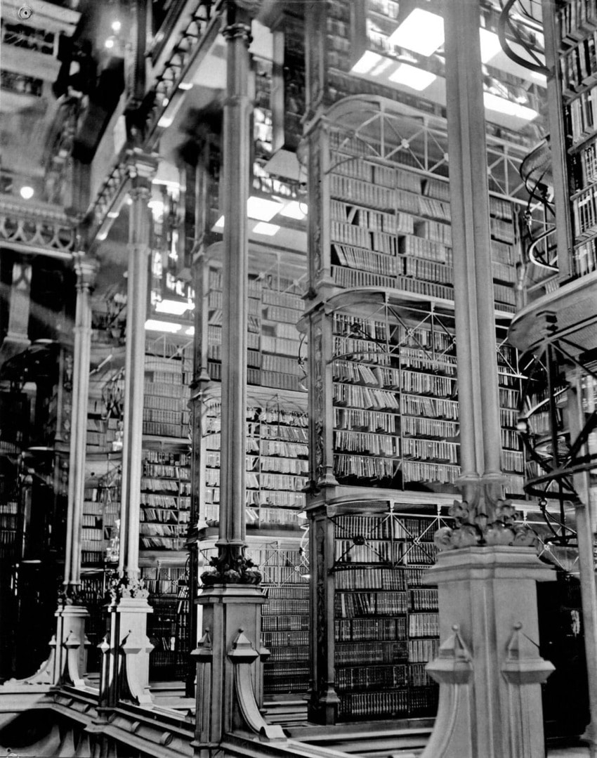Vintage library interior with towering shelves filled with books and ornate spiral staircases reaching multiple levels.