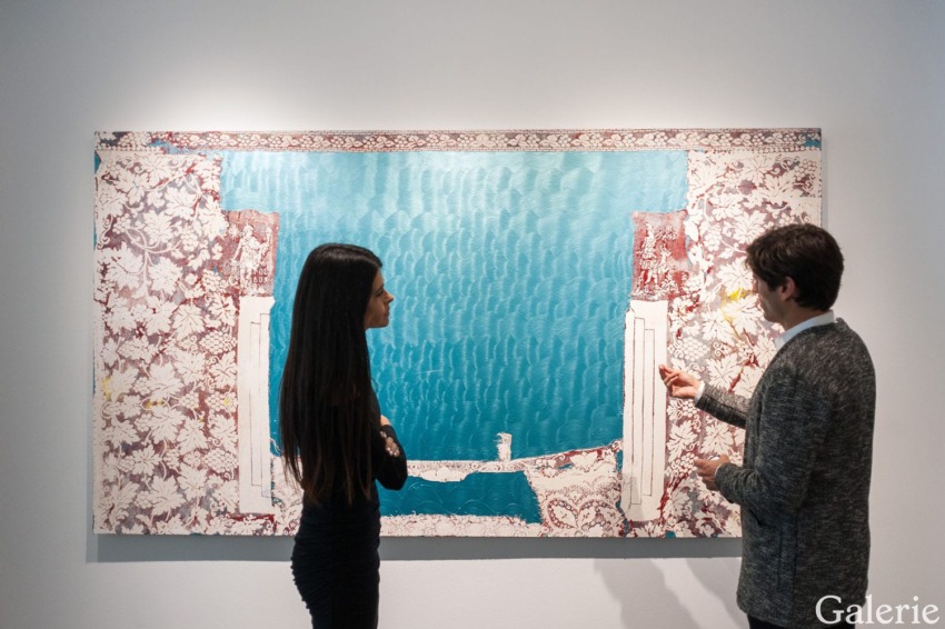 Two people discussing an abstract artwork featuring floral patterns and blue hues in a gallery setting.