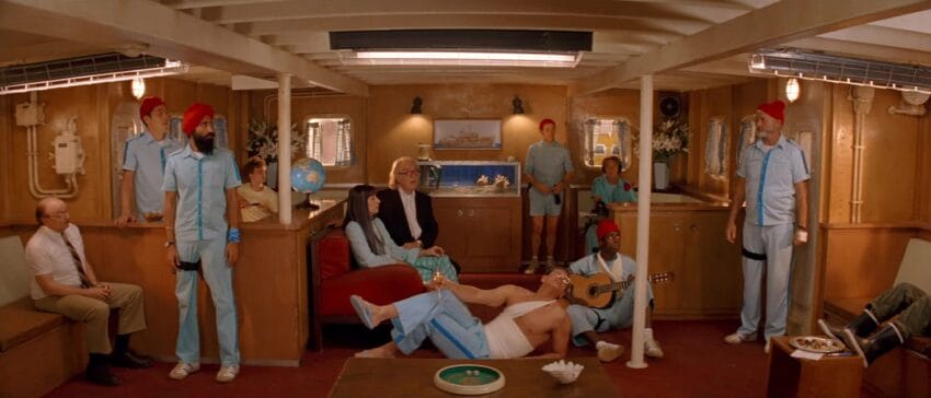 Group of people in nautical attire inside a ship's cabin, with one person playing guitar and others seated and standing around.