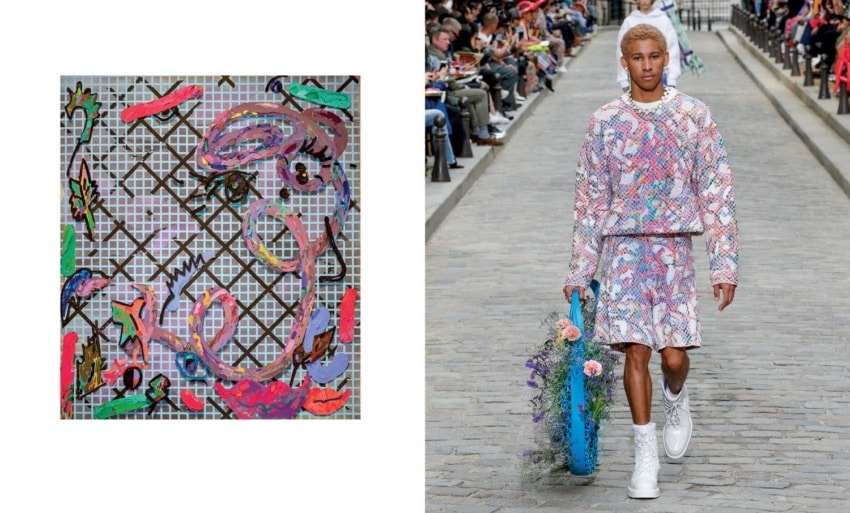 Fashion model in colorful patterned outfit walks runway holding floral accessory, with audience in the background.
