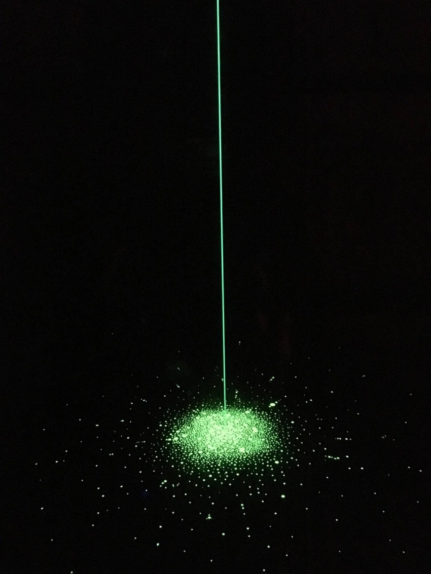 Green laser beam illuminating a field of glowing particles in darkness.