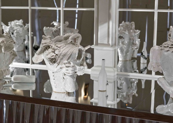 Decorative white porcelain sculptures and bottles on a mirrored shelf display in an elegant setting.