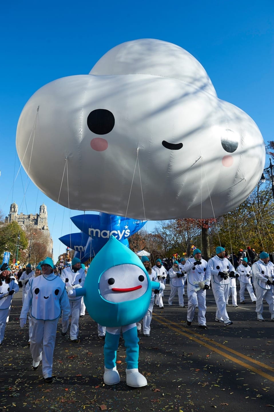 Cloud-shaped balloon floats above costumed parade participants in a festive outdoor event.