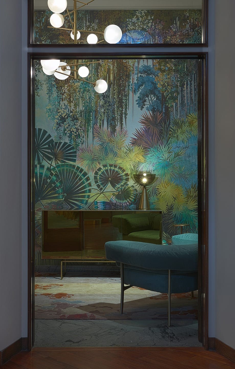 Elegant room with jungle-themed wallpaper, modern furniture, spherical light fixture, and a decorative lamp on a wooden cabinet.