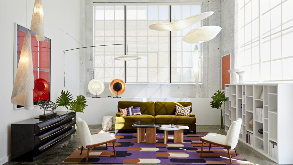 Modern living room with abstract lighting, green sofa, geometric rug, wooden table, and large windows.