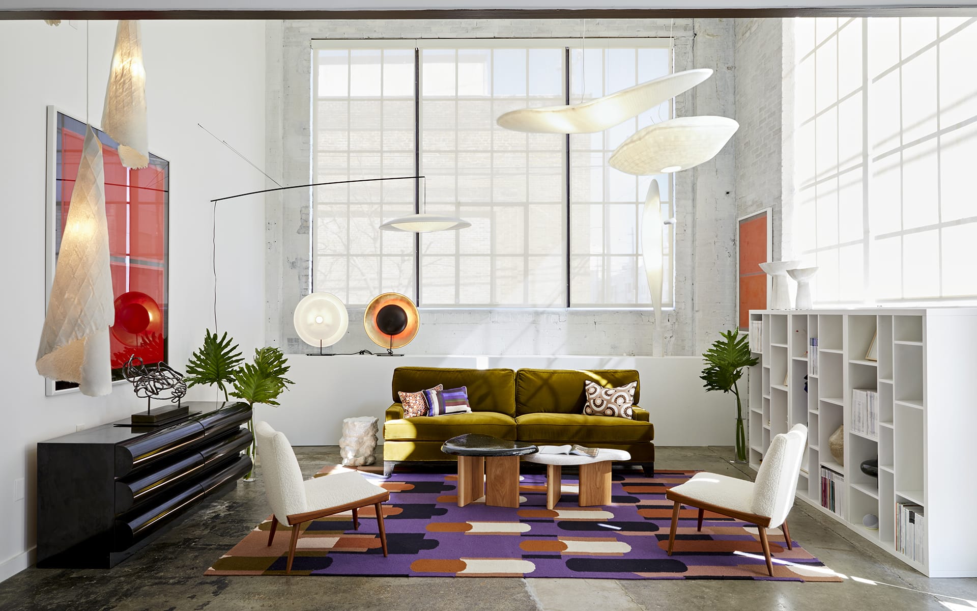 Modern living room with abstract lighting, green sofa, geometric rug, wooden table, and large windows.