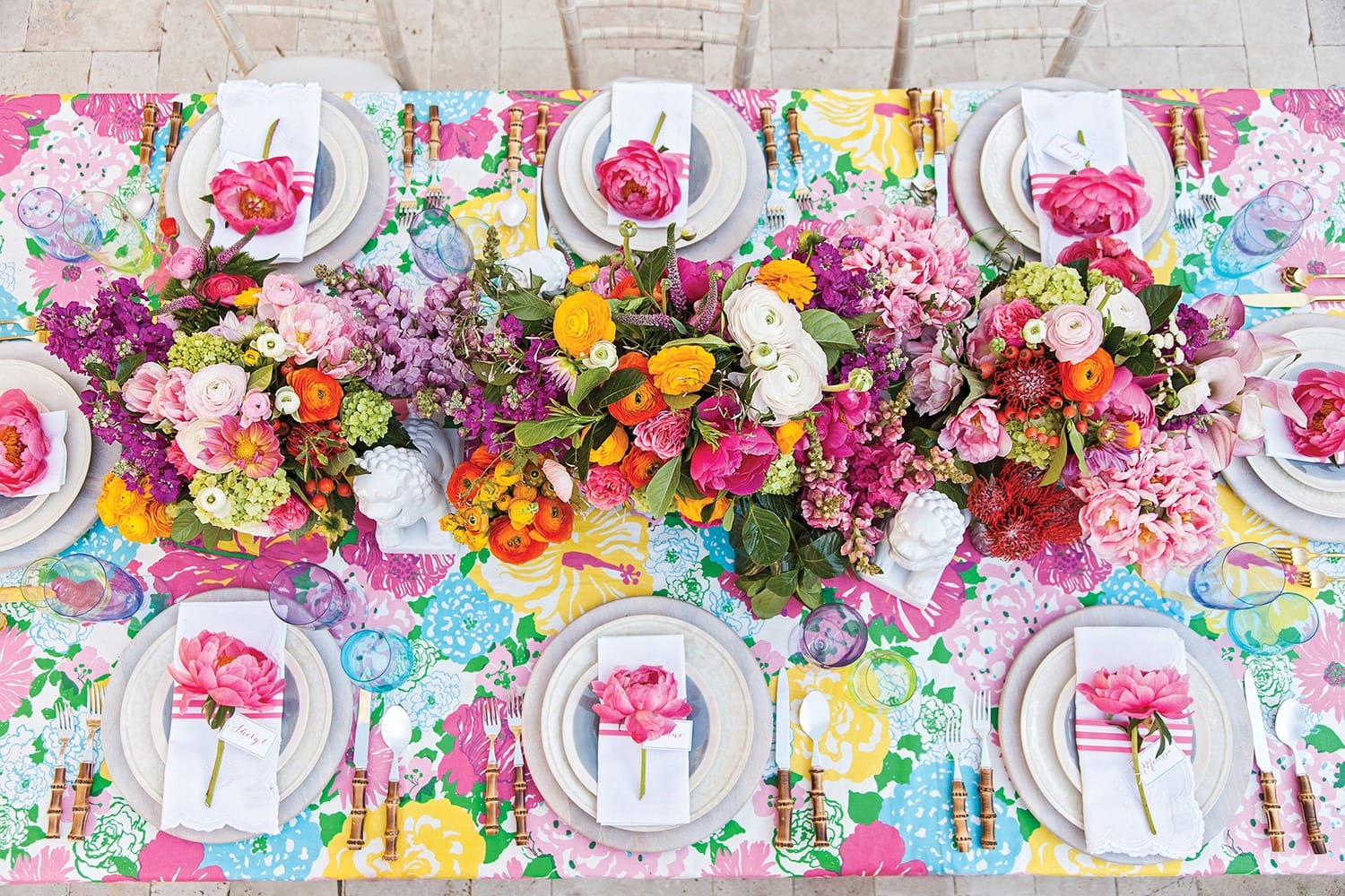 Colorful floral table setting with plates, napkins, and vibrant flower arrangements on a patterned tablecloth.