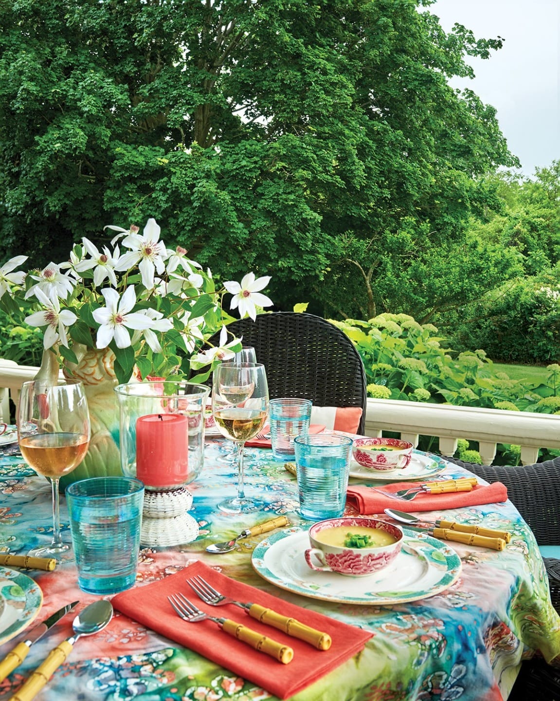 Colorful outdoor dining table set with floral centerpiece, assorted glassware, and vibrant tableware on a patio.