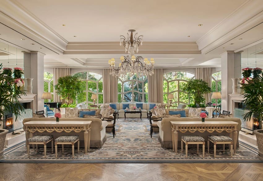 Elegant hotel lobby with luxurious sofas, chandeliers, large windows, and indoor plants, creating a sophisticated ambiance.