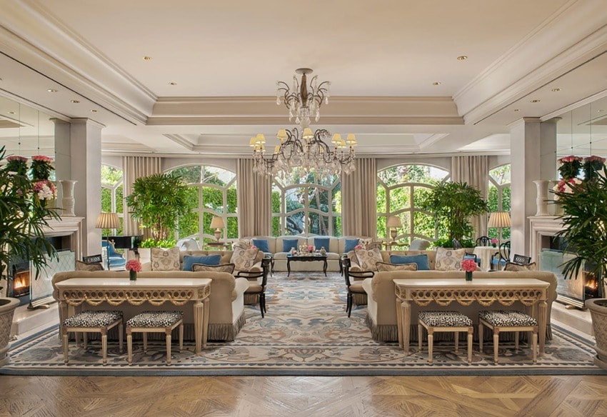 Elegant hotel lobby with luxurious sofas, chandeliers, large windows, and indoor plants, creating a sophisticated ambiance.