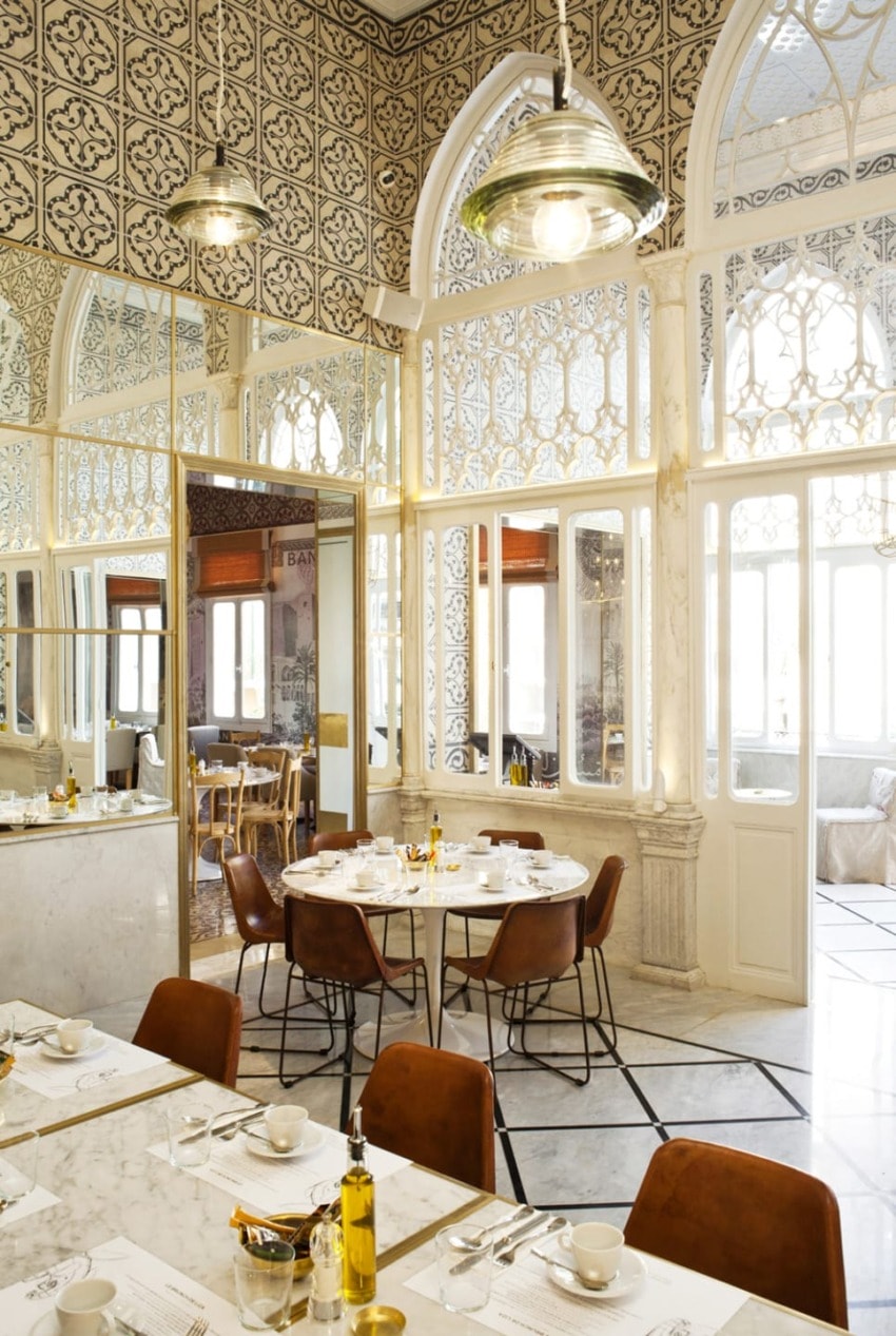 Elegant restaurant interior with ornate tile walls, arched windows, and marble tables set for dining, creating a luxurious atmosphere.