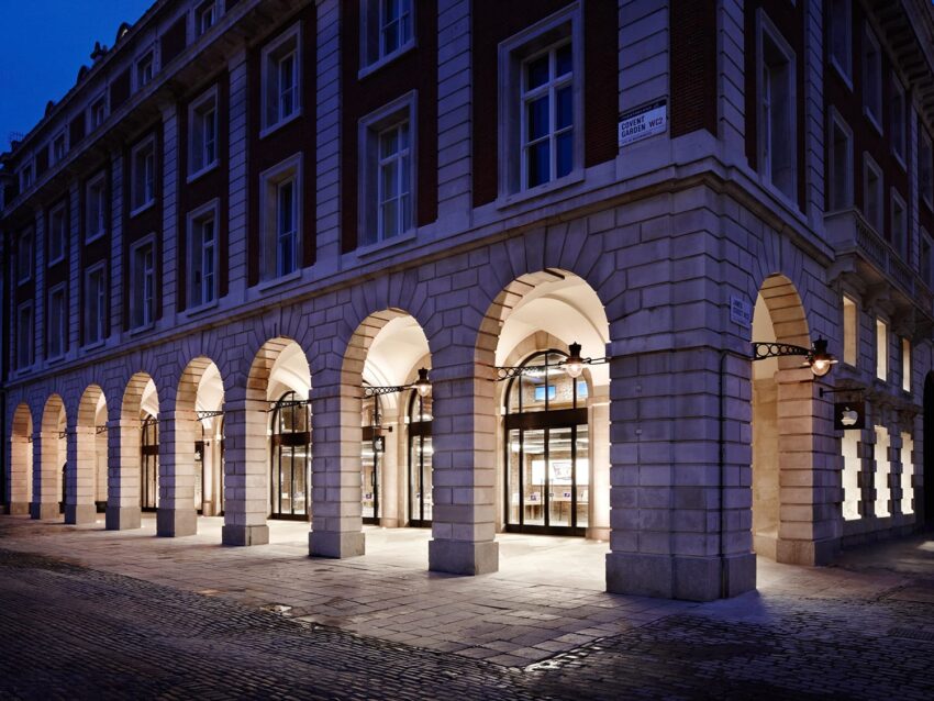 Illuminated arched building entrance with cobblestone path at night.