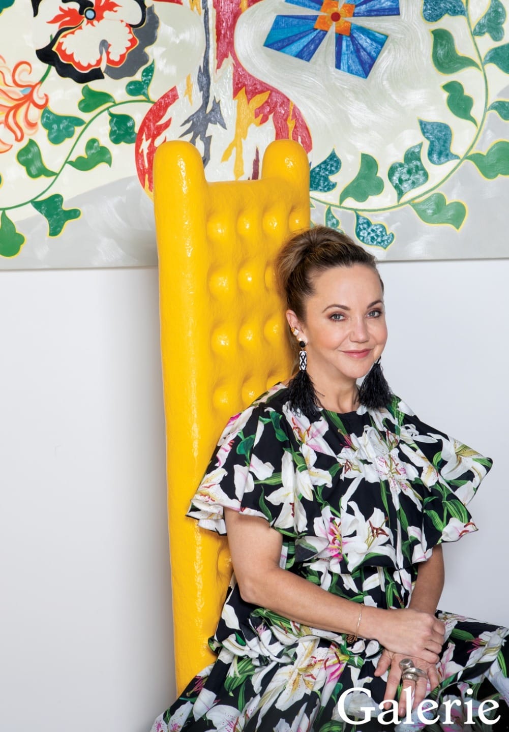 Person seated in a floral dress on a yellow chair with colorful art in the background.