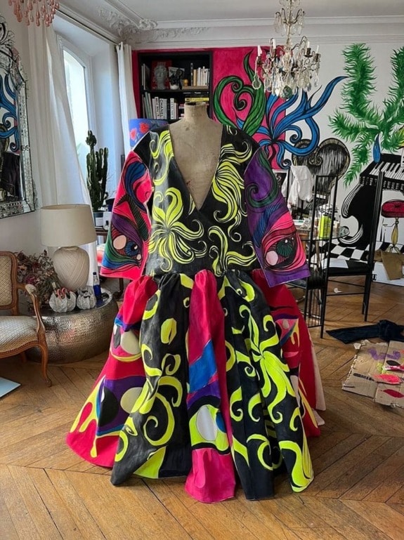 Colorful, abstractly painted dress on mannequin in creatively decorated room with wooden floor and vintage furniture.