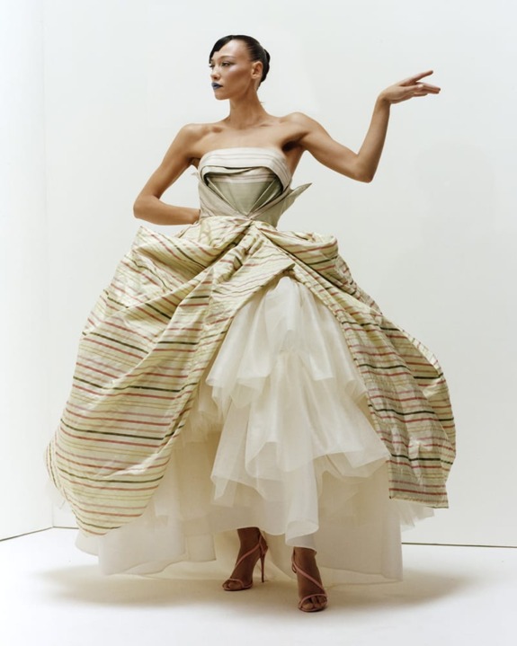 Person wearing a strapless, striped gown with layered tulle skirt, striking a pose against a plain background.