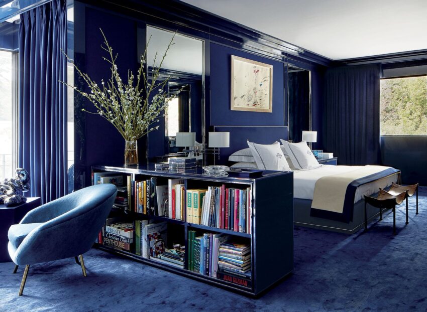 Luxurious navy blue bedroom with a bookshelf, modern decor, large mirror, and elegant seating.