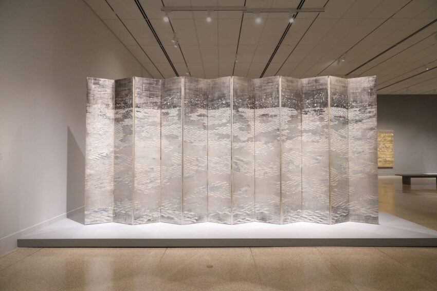 Japanese folding screen with intricate white and gray patterns on display in a modern art gallery setting.