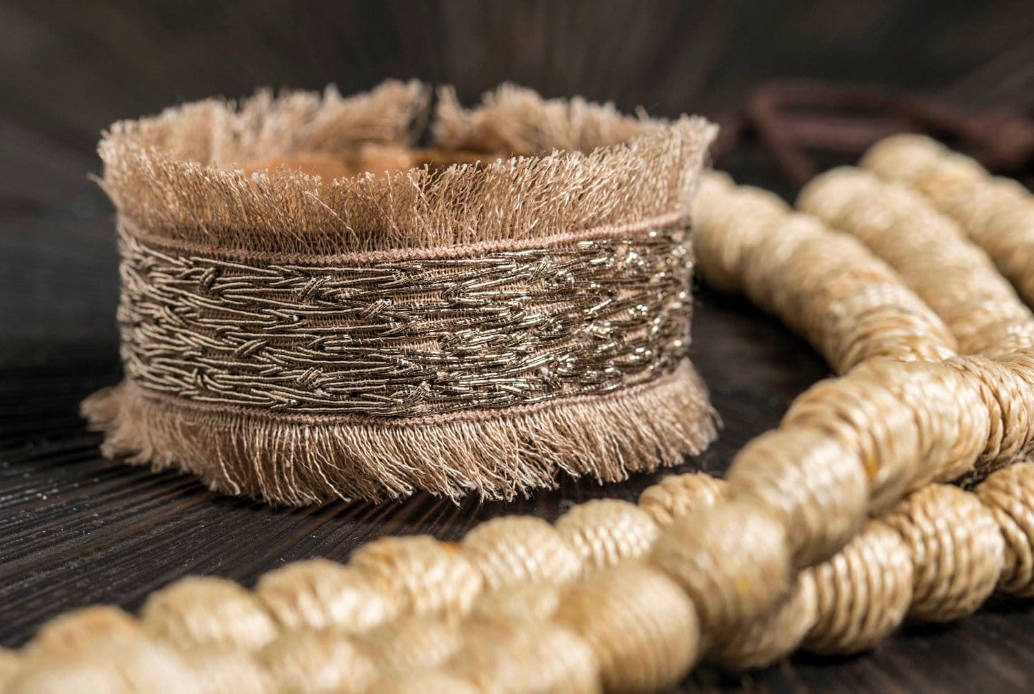 Close-up of a textured beige bracelet with intricate weaving, placed next to a coiled natural fiber rope.