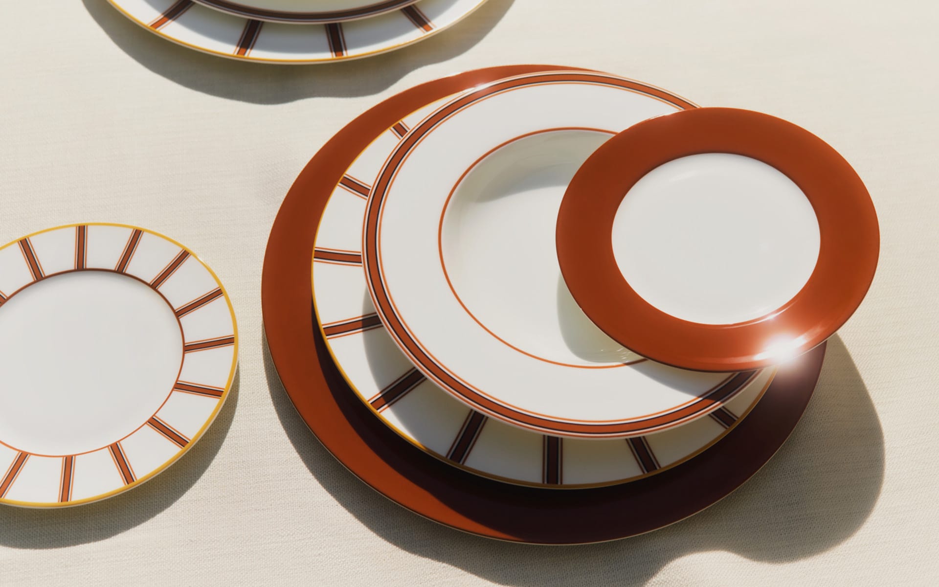 Stacked plates with brown and white patterns on a beige surface, sunlight reflecting off the top plate.