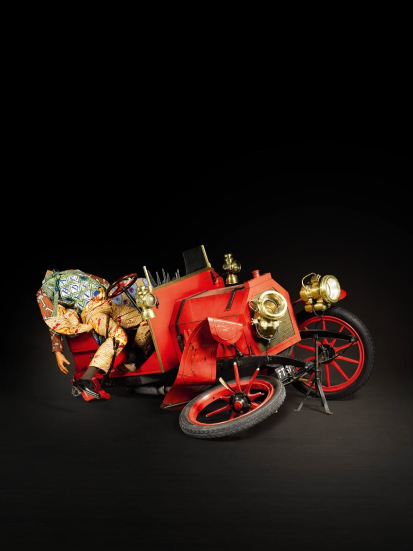 A creatively designed red vintage car with a whimsical, colorful human figure appearing to interact with the vehicle.