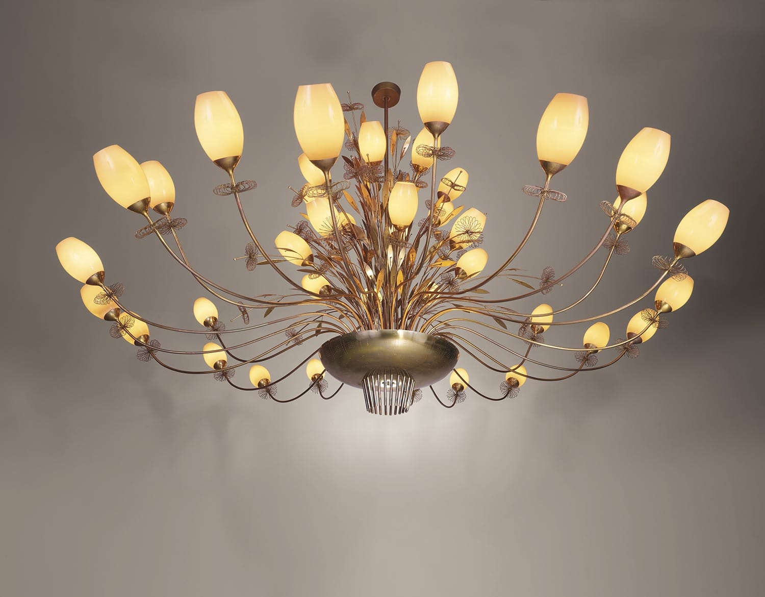 Elegant, modern chandelier with numerous glowing bulb fixtures arranged on curved metal arms, against a neutral background.