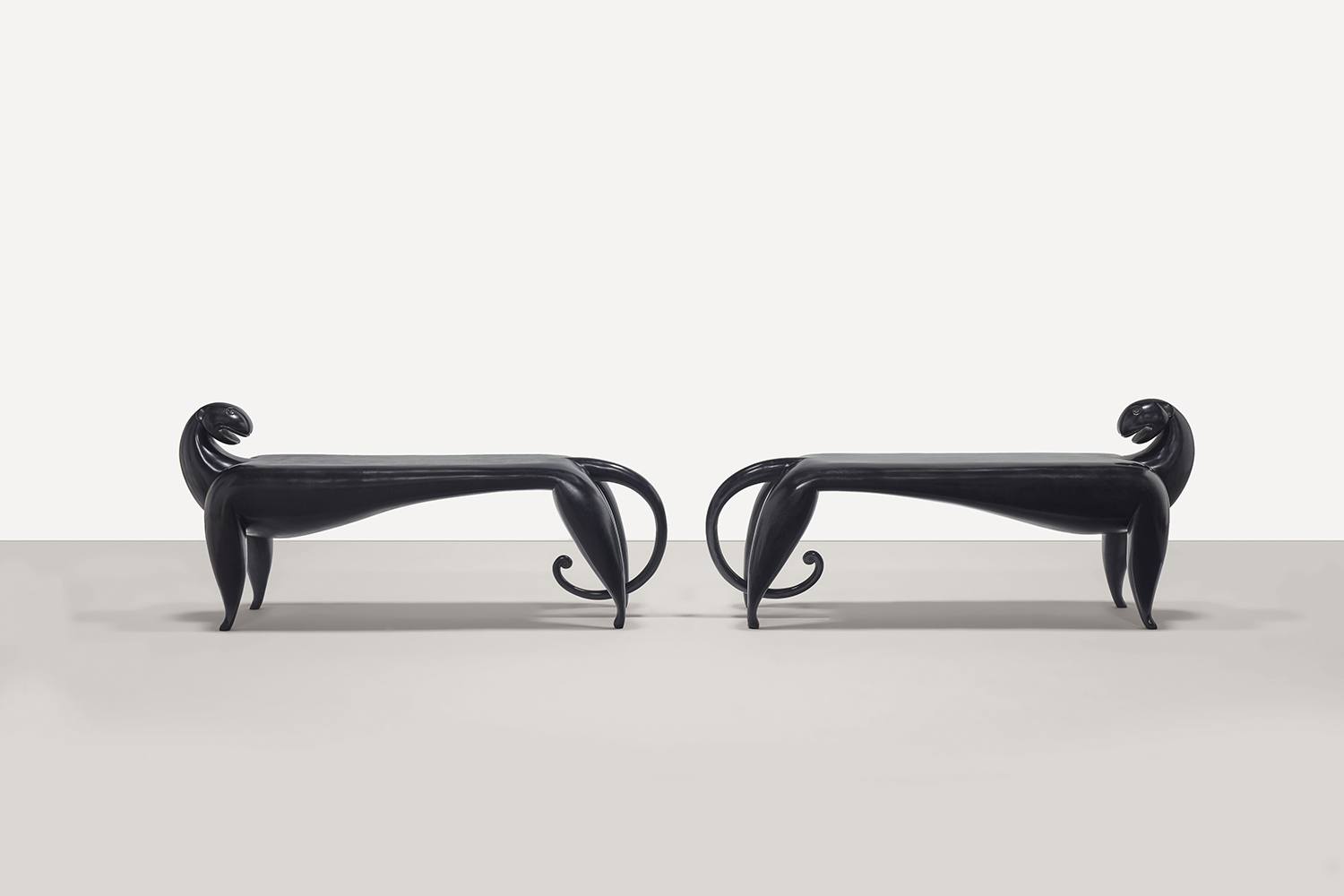 Two black, sculptural benches shaped like stylized animals facing each other in a minimalist setting.