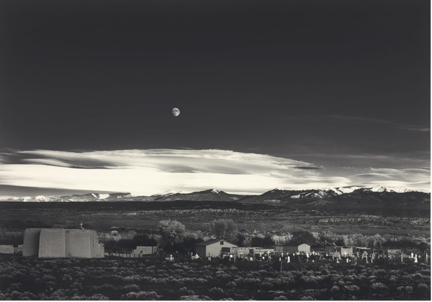 Black and white landscape of a church with distant mountains under moonlit sky.