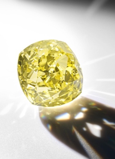 Yellow diamond resting on a reflective surface with a prism-like light effect.