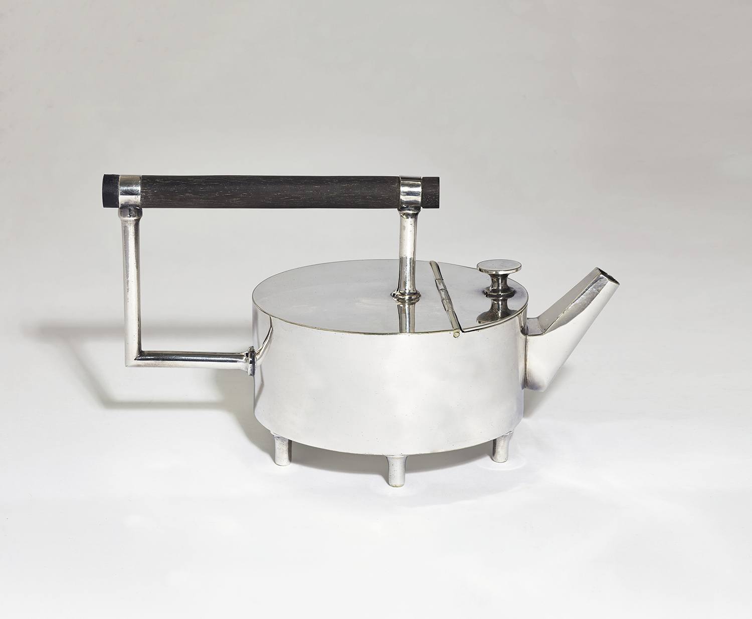 Silver modernist teapot with geometric design and black handle on a plain background.