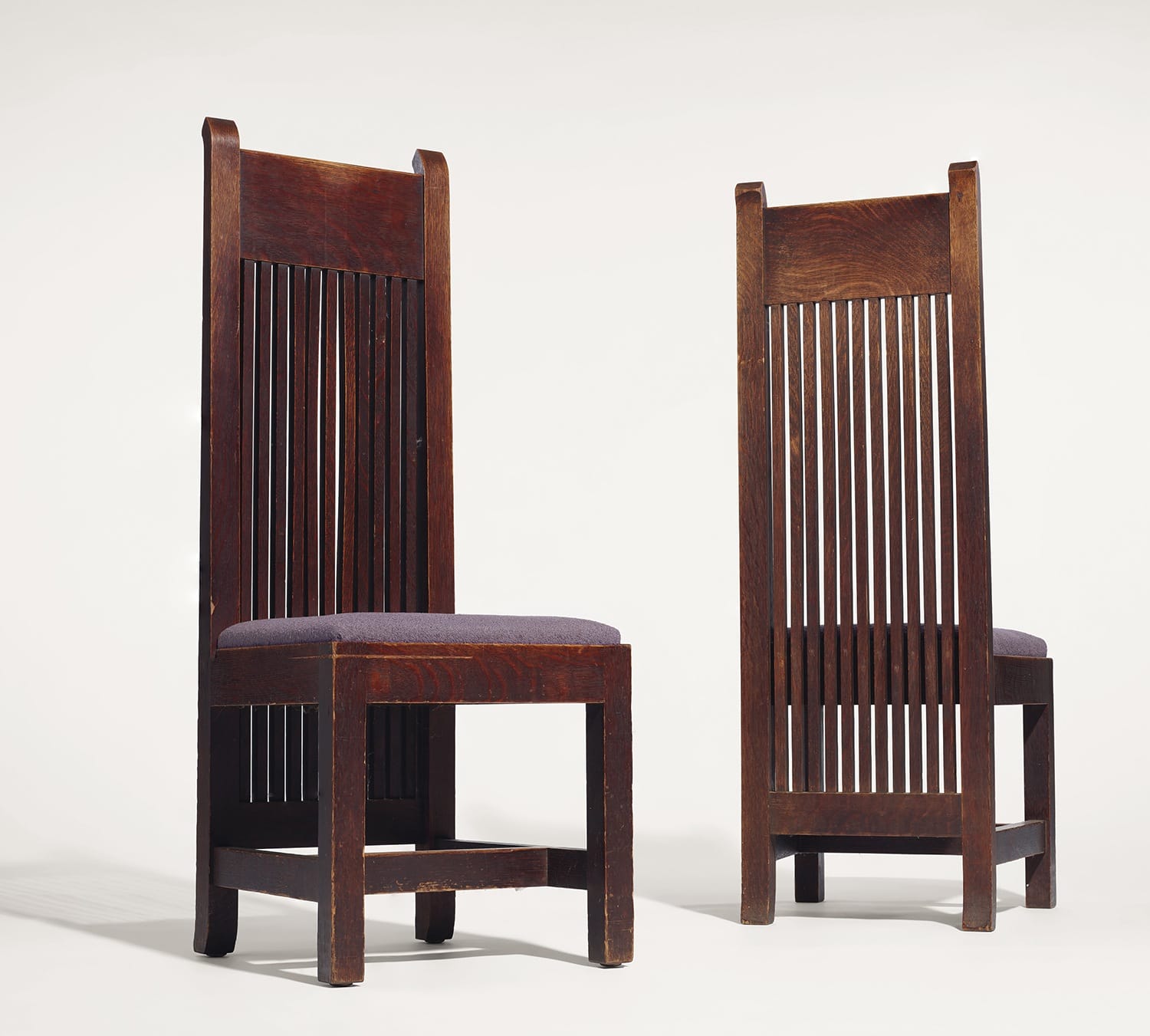 Two wooden high-back chairs with vertical slat designs, upholstered seats, and sturdy legs on a plain background.