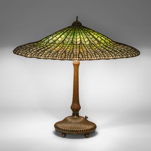 Vintage table lamp with a wide green stained glass shade and bronze base, casting a warm light.