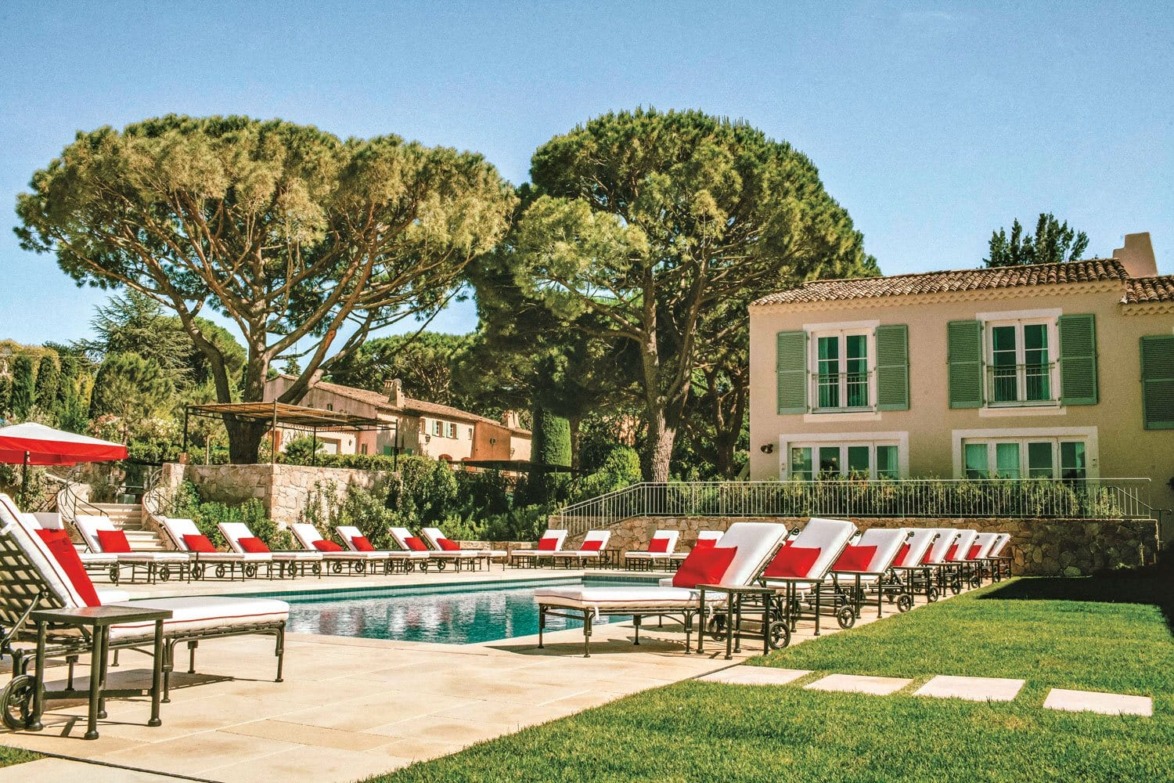 Luxury outdoor pool area with lounge chairs surrounded by lush greenery and a large villa in the background.