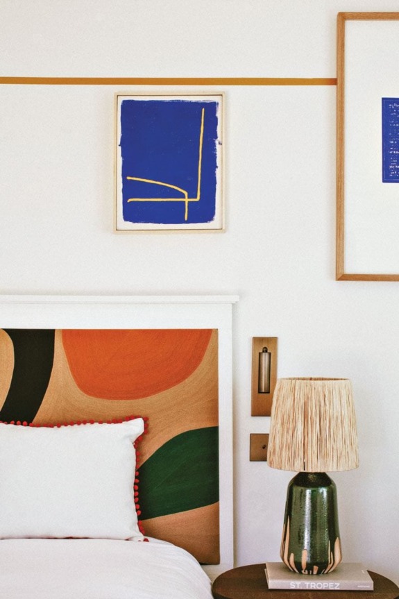 Stylish bedroom with colorful abstract wall art, wooden headboard, and a decorative lamp on a side table.
