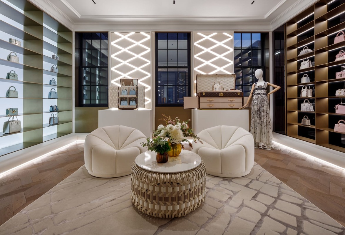 Luxurious boutique interior featuring elegant seating, flower arrangement on a table, and shelves displaying designer handbags.
