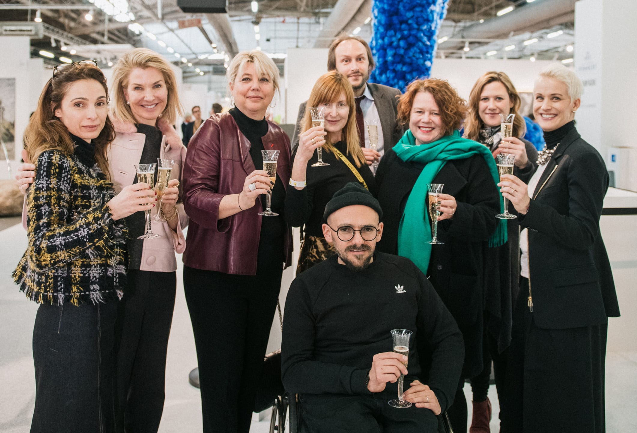 Group of people smiling, holding champagne glasses in an indoor setting, casual and formal attire.