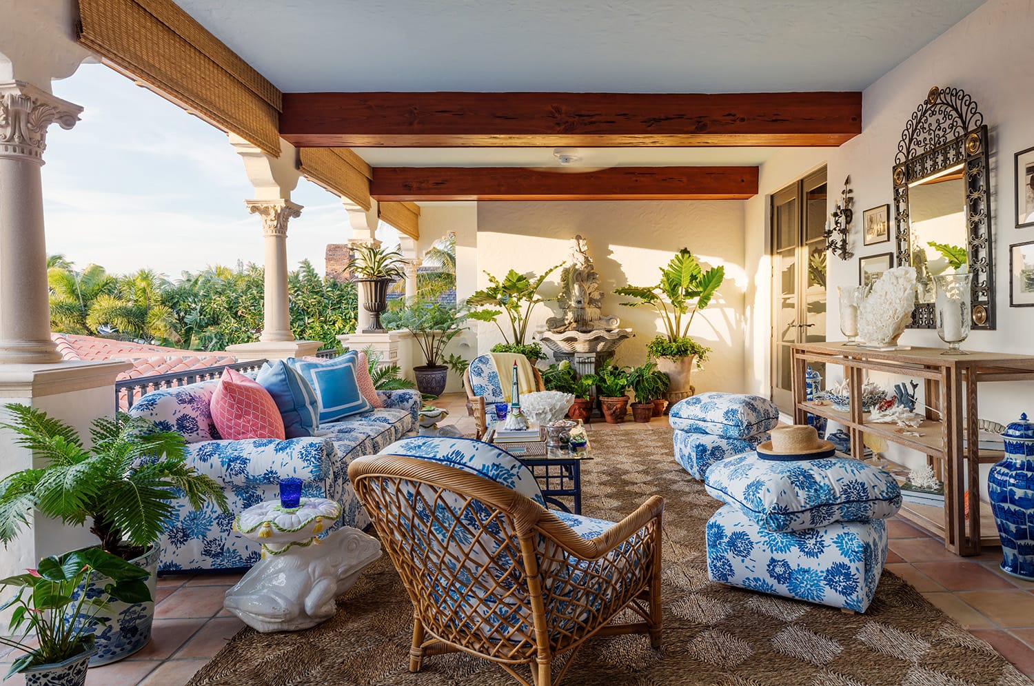 Outdoor patio with blue and white furniture, wicker chair, decorative plants, and a fountain under wooden beams.
