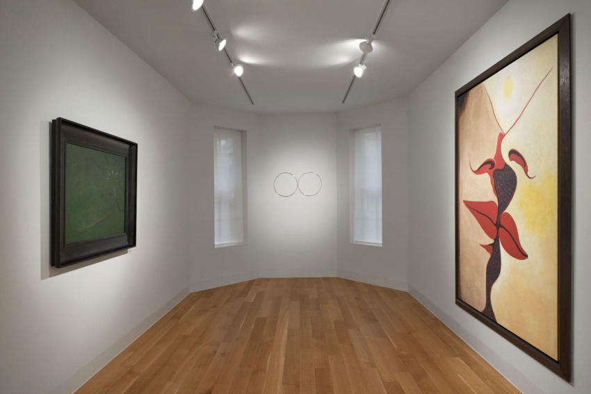 Minimalist art gallery with paintings on white walls, wooden floor, and spotlights highlighting abstract artwork.