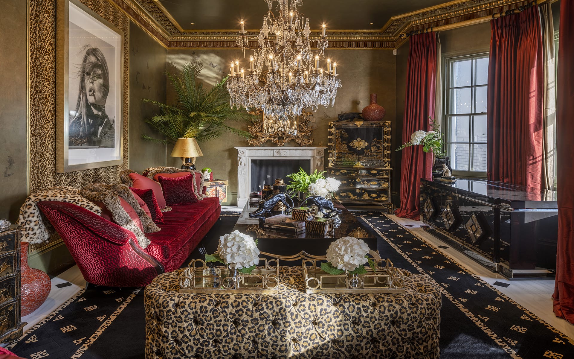 Luxurious living room with chandelier, red velvet sofa, leopard print accents, and opulent decor elements.